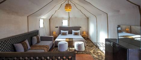 A tent-style room with a bed, two bedside tables, a sofa, and a TV.