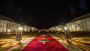 A carpeted pathway leading to tents with lanterns on either side. - DWO Golden Camp Merzouga (Taouz)