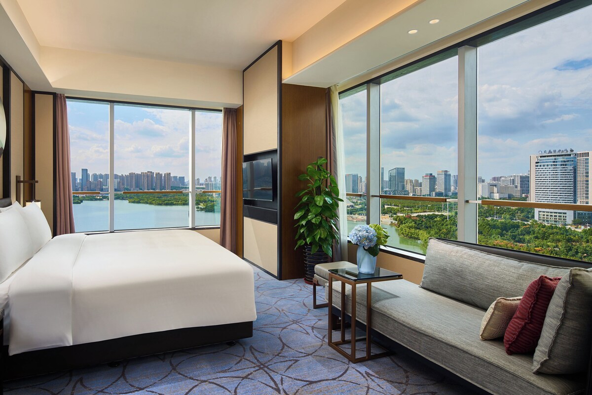 Habitación de hotel con una cama grande, un sofá, un televisor y vistas a la ciudad y al agua.
