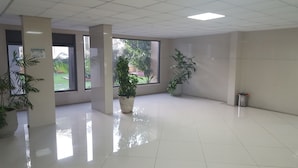 Un hall d’entrée spacieux, doté de grandes fenêtres, de plantes en pot et d’un sol carrelé.