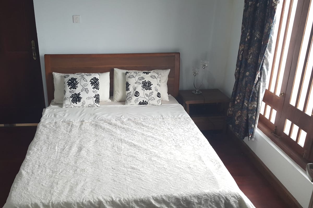 A neatly made bed with floral-patterned pillows, a wooden headboard, and a bedside table with a lamp.