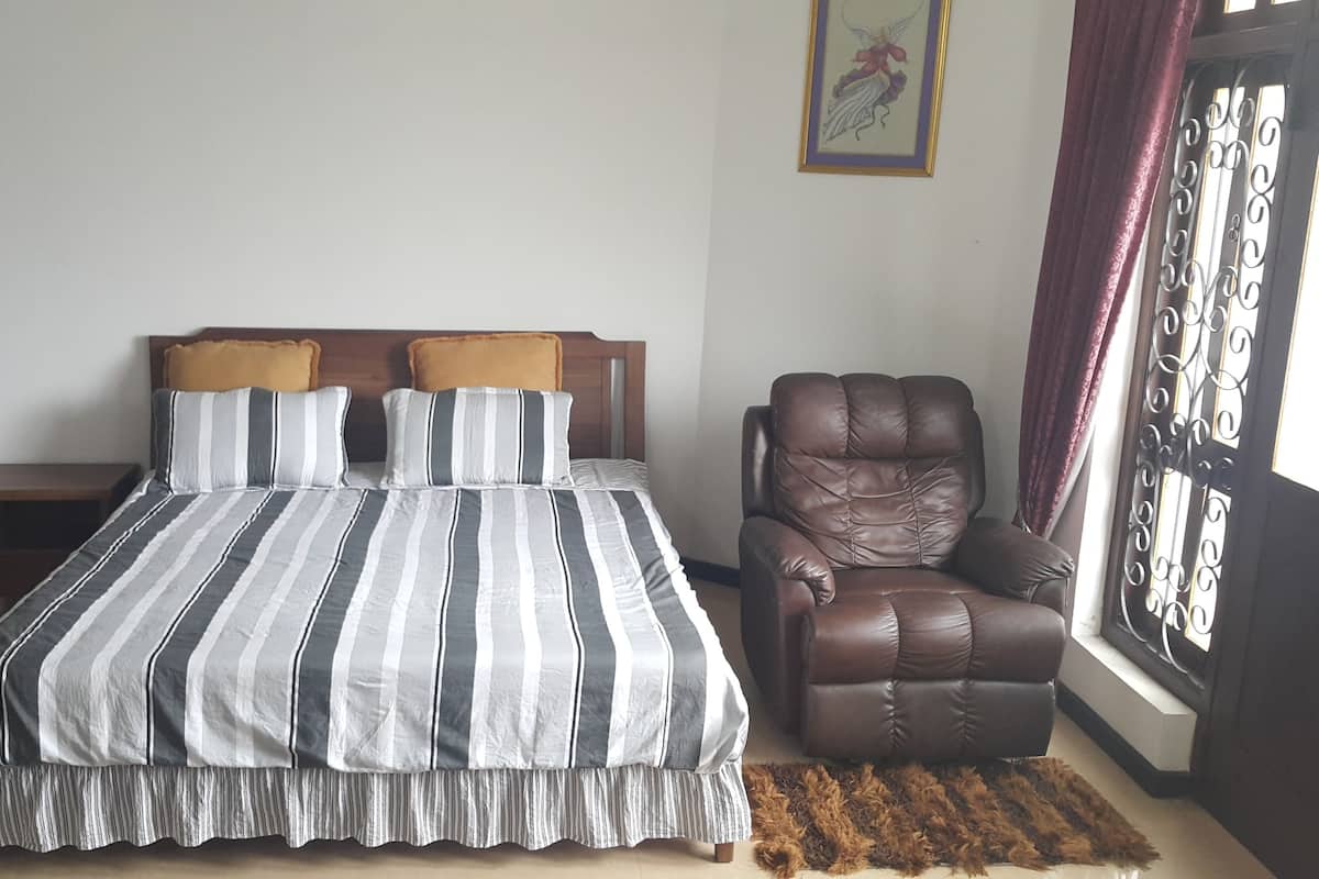 A bedroom with a bed, a chair, and a window with curtains.