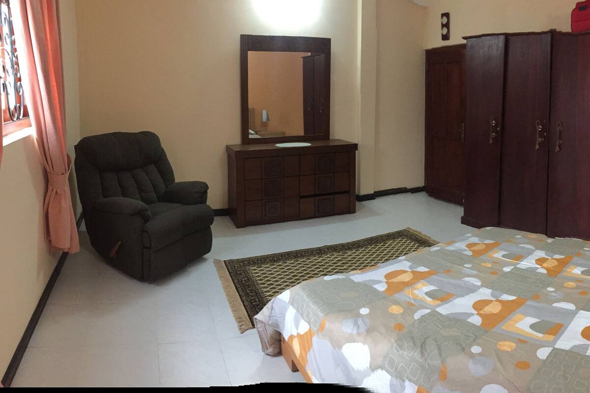 A bedroom with a bed, a wardrobe, a chair, and a mirror.