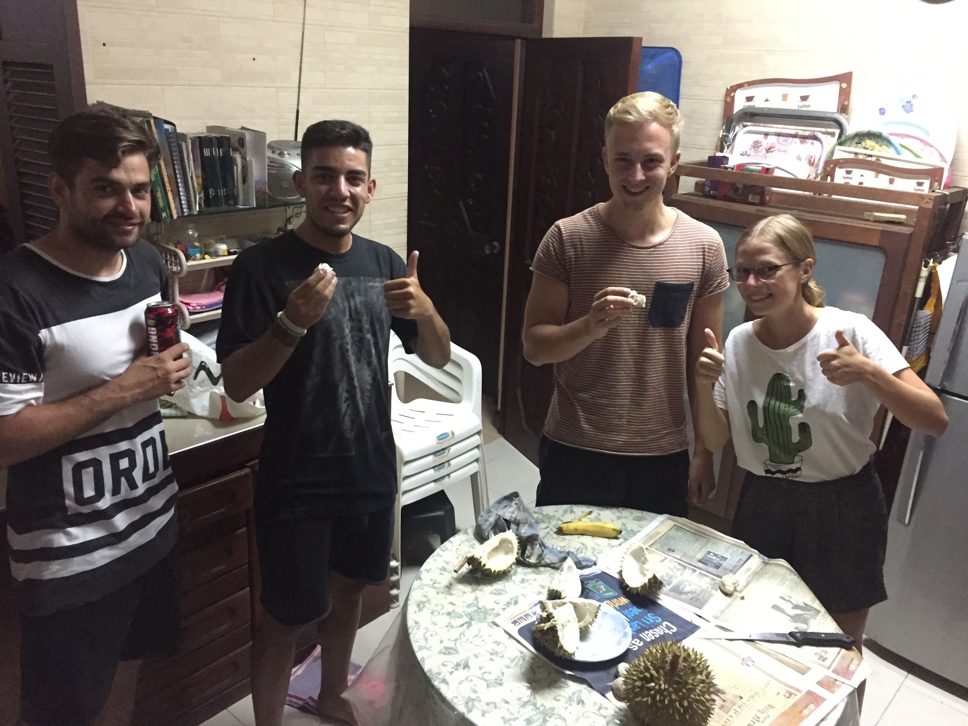 A group of people in a kitchen area with a dining table, chairs, and various kitchen appliances.