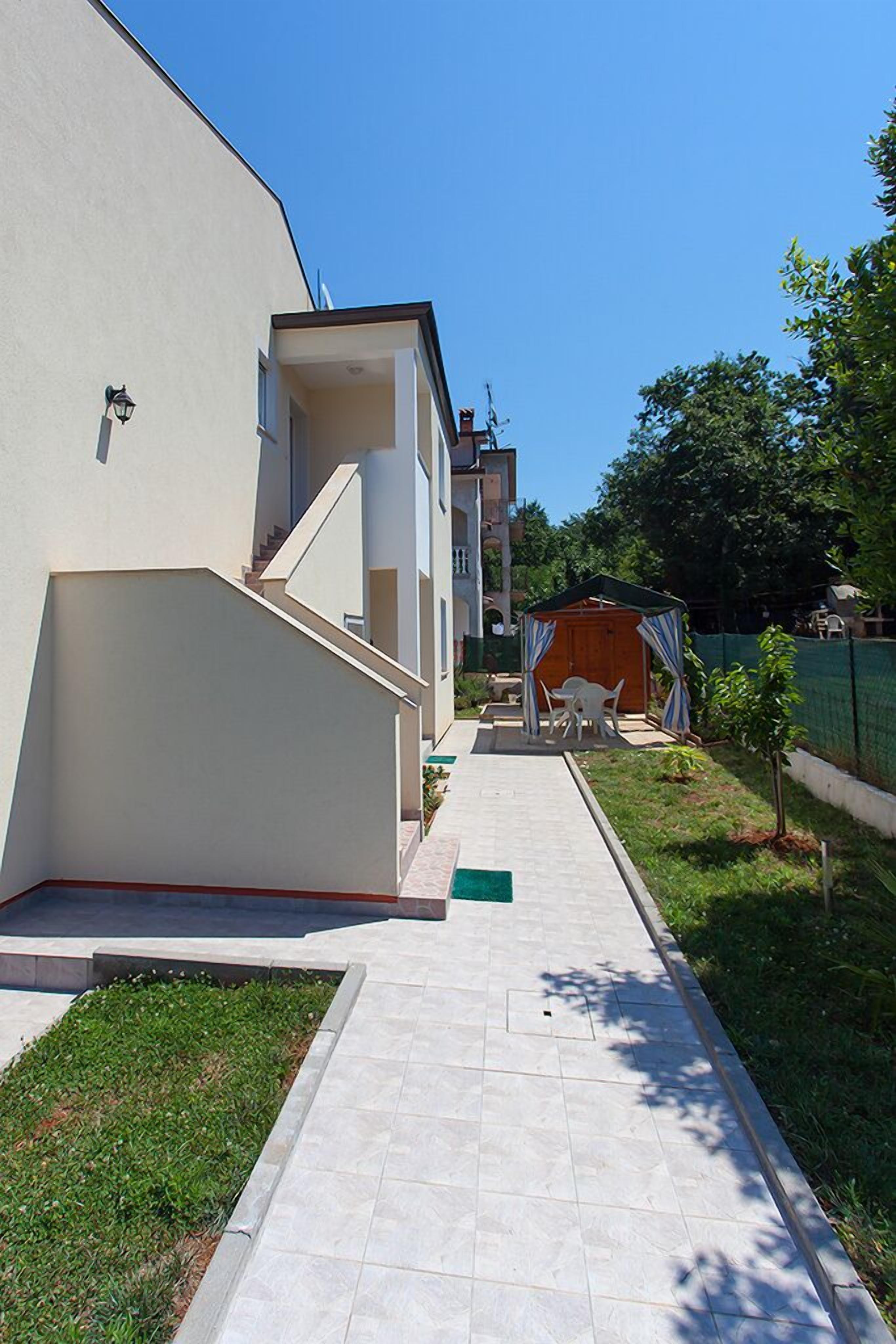 A residential building with a paved pathway leading to a covered outdoor seating area.