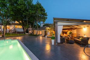 A modern outdoor patio with a swimming pool, a covered seating area, and a well-lit interior space. - Felix Residence (Porec)