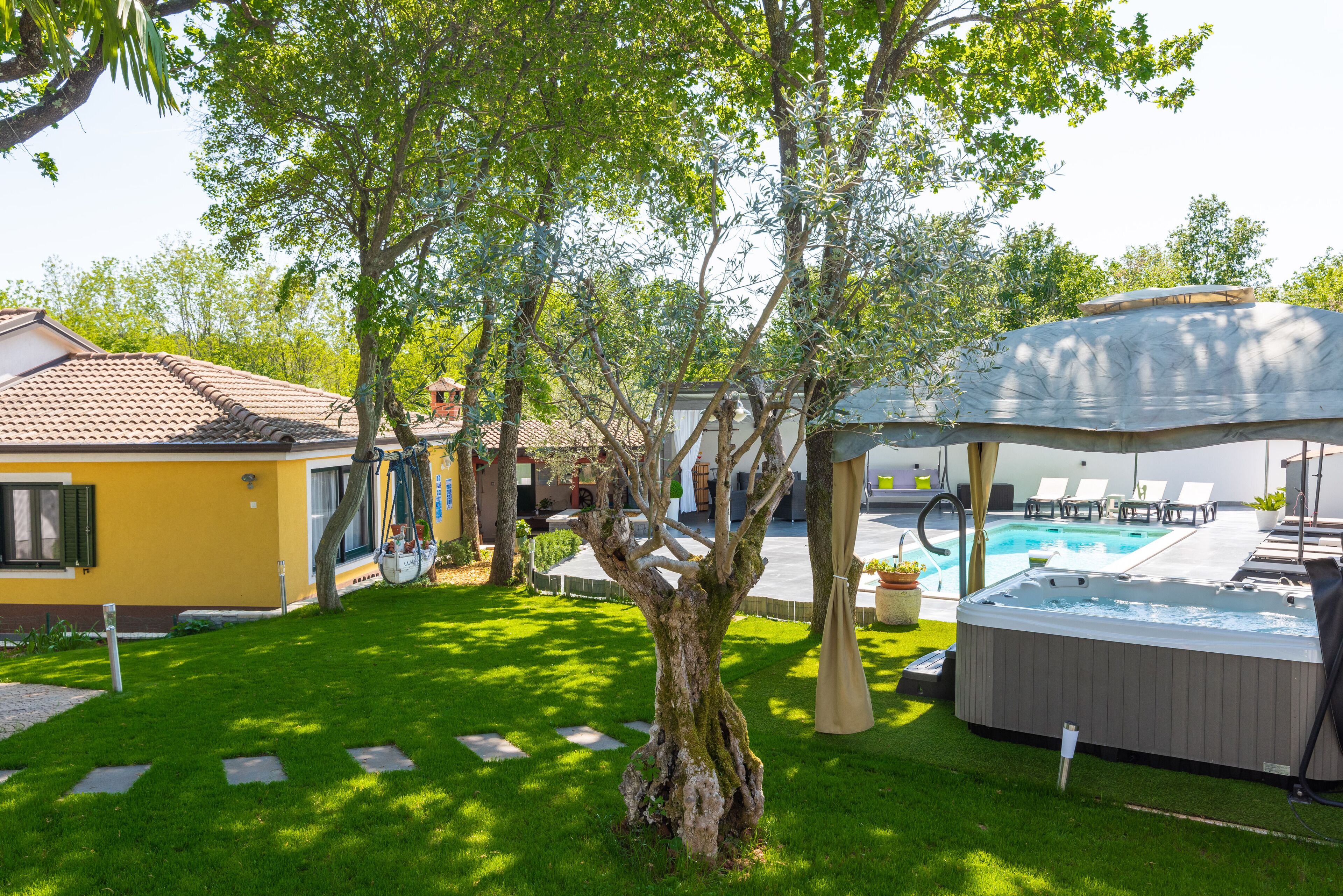 A backyard with a swimming pool, hot tub, and a covered seating area.