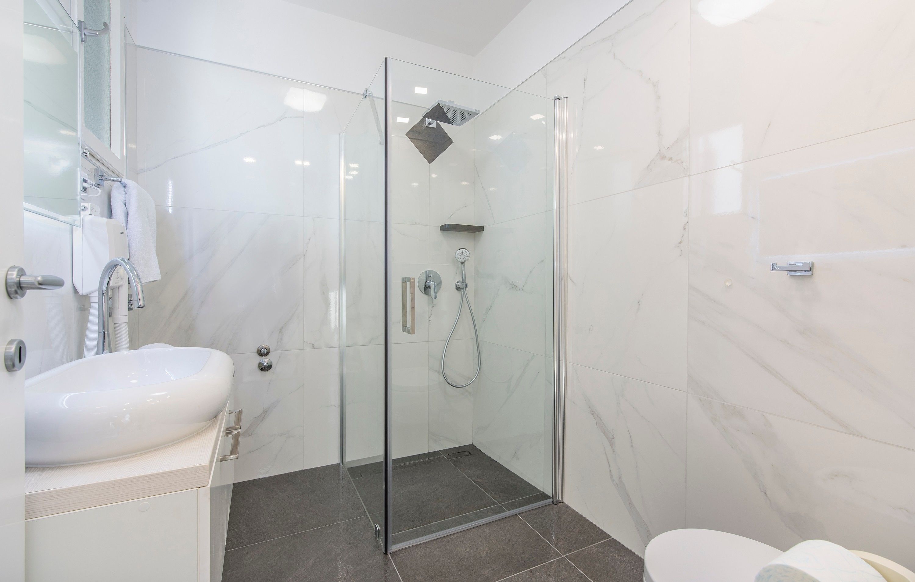 Un baño moderno con cabina de ducha de vidrio, un lavabo blanco y un inodoro.