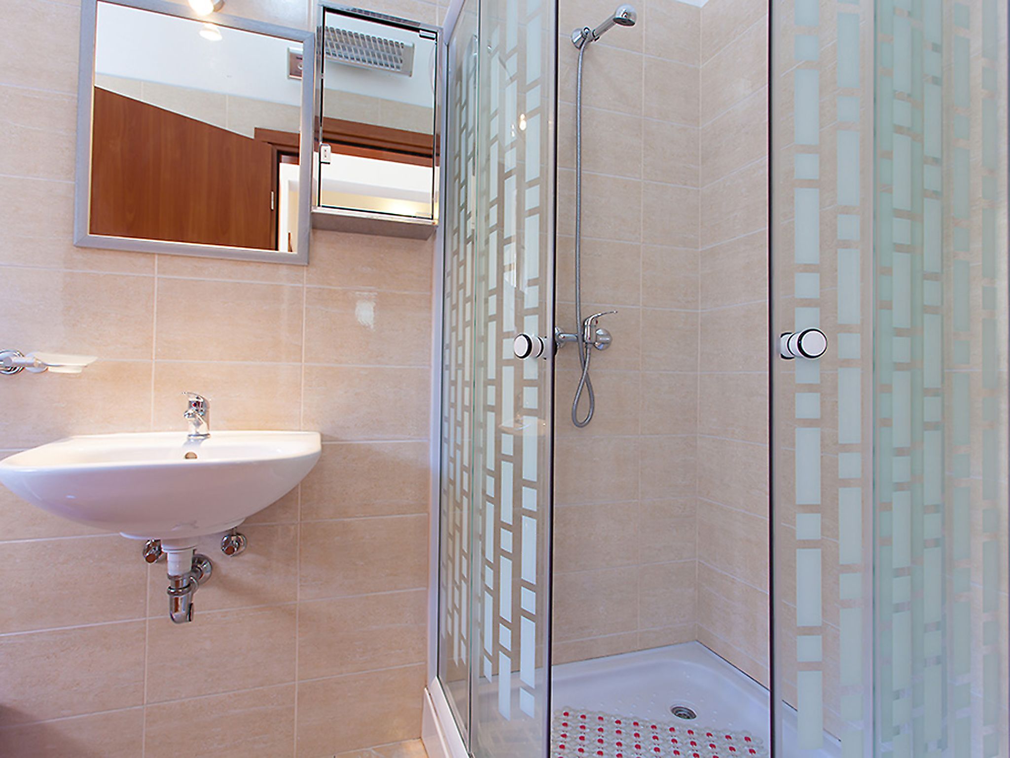 Un baño con lavamanos, espejo y ducha con mampara de vidrio.