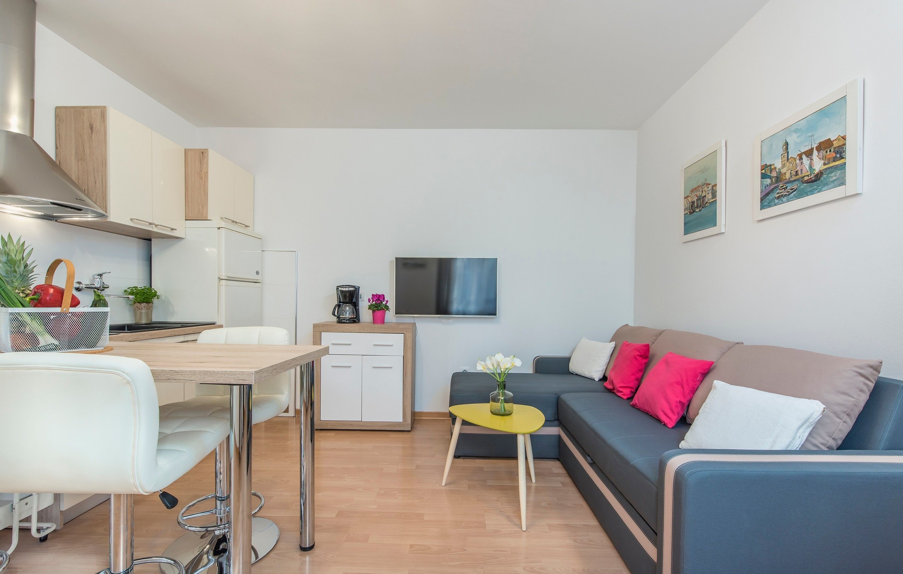 A modern kitchen with white cabinets, a dining table with chairs, a small coffee table, and a sofa with colorful cushions.