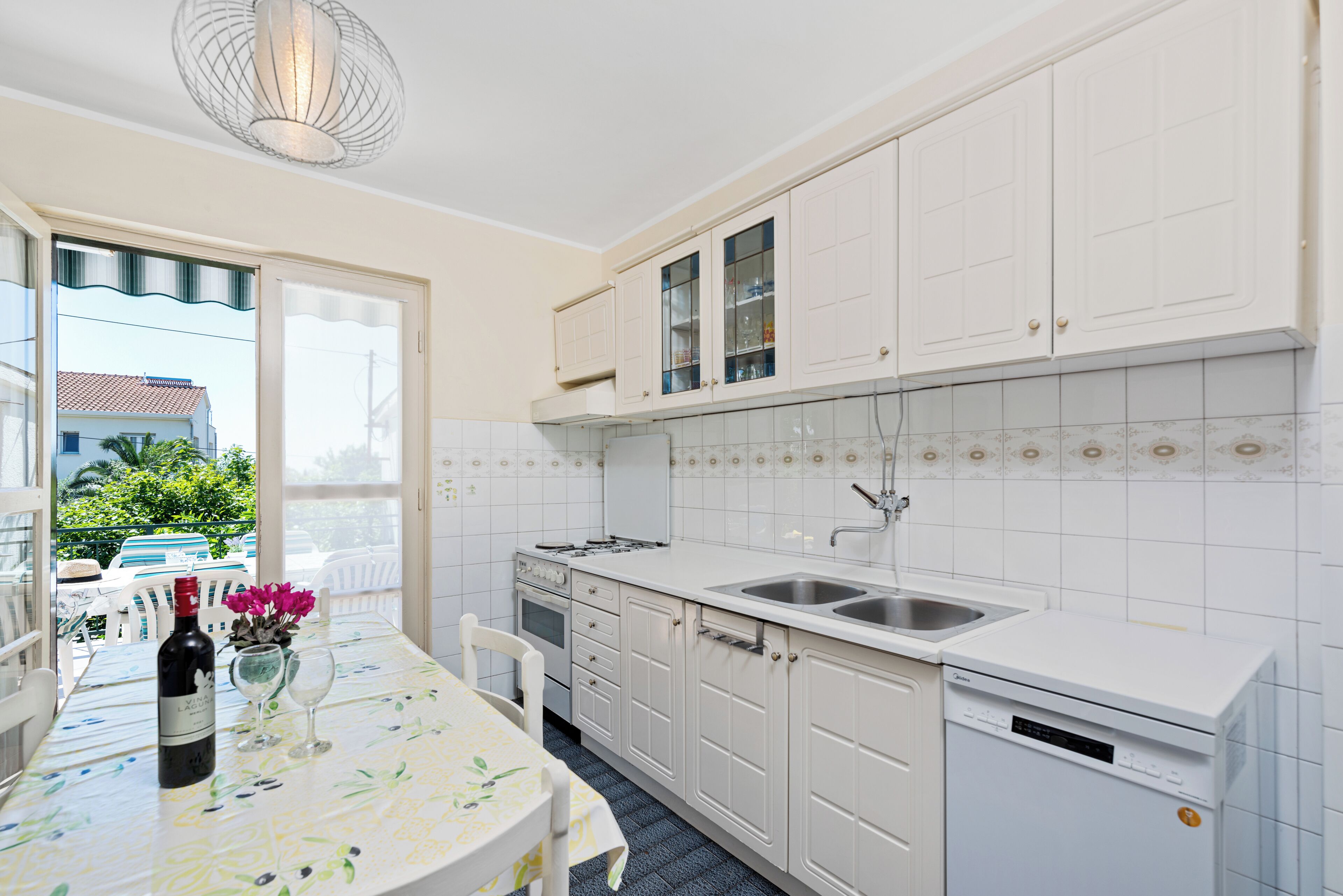 A kitchen with white cabinets, a sink, a dishwasher, and a dining area with a table and chairs.