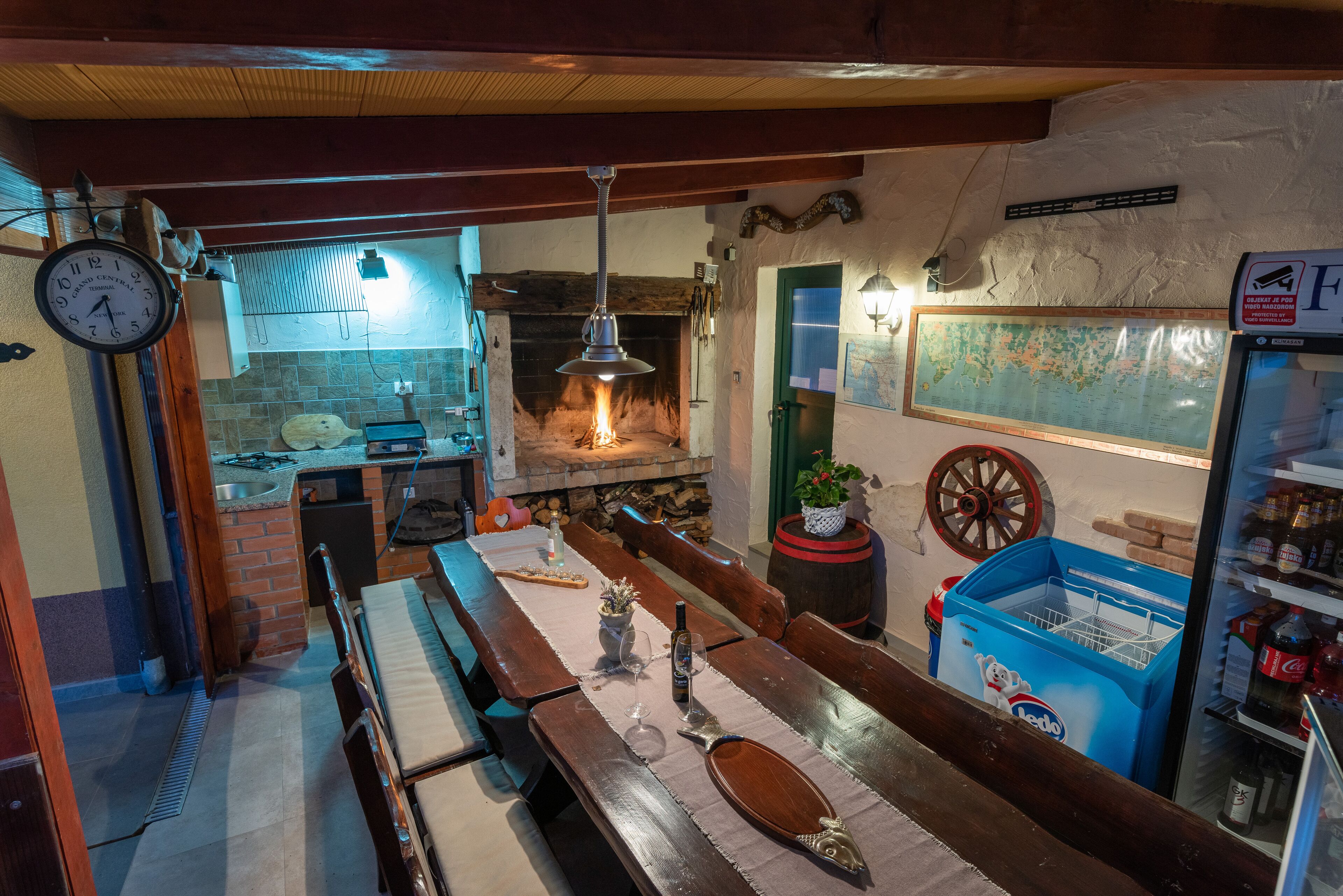A rustic kitchen with a brick wall, wooden benches, a hanging light fixture, and a large map on the wall.
