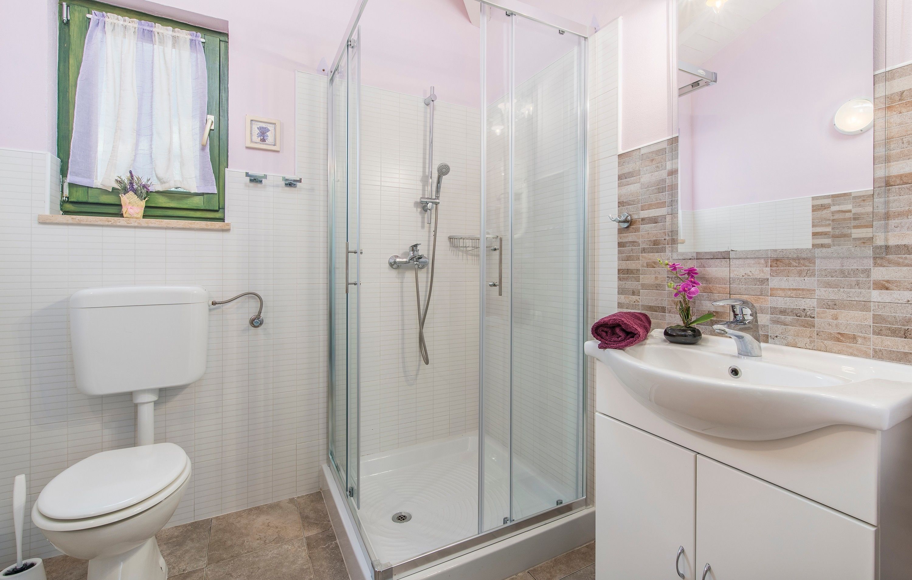 Un baño con ducha de vidrio, inodoro blanco, lavamanos con espejo y ventana con cortina.