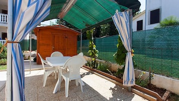 Ein Patio mit einem Holztisch und weißen Plastikstühlen unter einem gestreiften Markisenvorzelt.