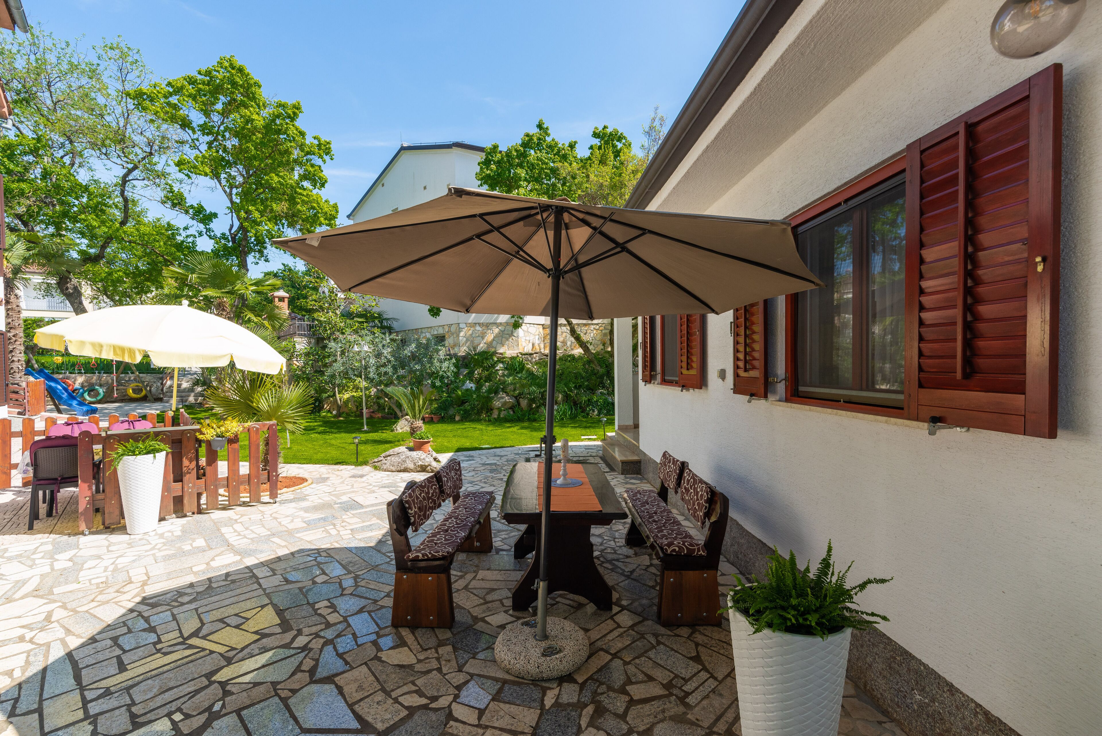 An outdoor patio with a stone floor, a table with benches, and two umbrellas.
