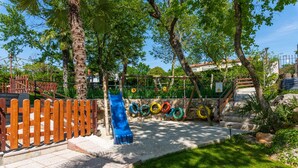 A playground with a slide, tire swings, and a wooden fence. - Felix Residence (Porec)