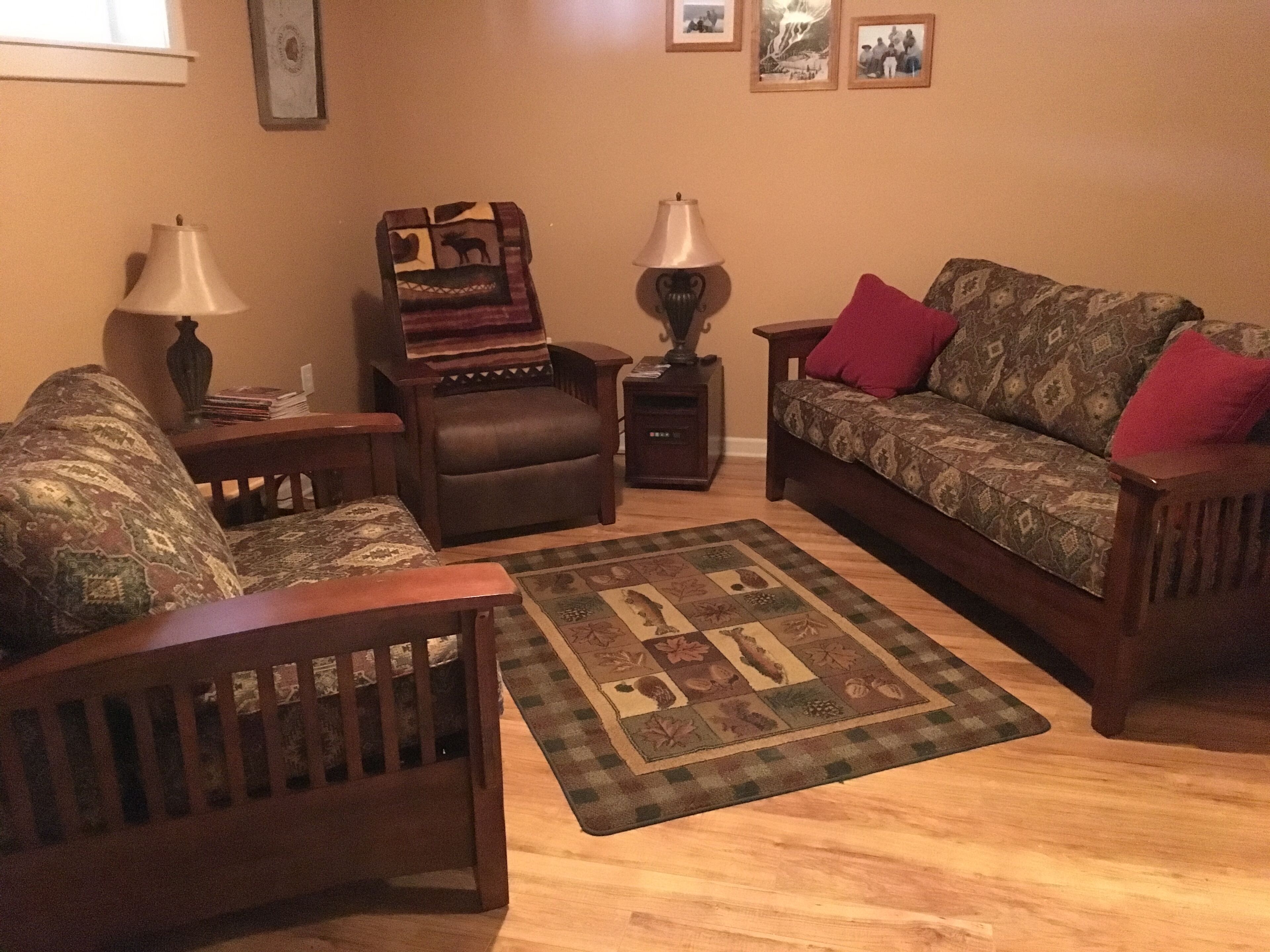Een woonkamer met een houten salontafel, twee fauteuils, een bank en een kamerkleed met dessin.