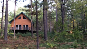 Una cabaña con terraza y un ventanal grande, rodeada de bosque.
