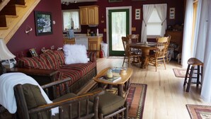 Un salón acogedor con un sofá, sillas, una mesa de centro y un comedor con mesa y sillas. Hay una zona de cocina con armarios de madera y una ventana.