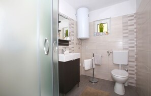 Een moderne badkamer met een glazen douchedeur, een witte wastafel, een donkere kast, een toilet en een handdoekhouder.