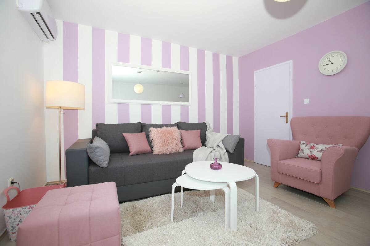 Una sala de estar con un sofá gris, un sillón rosa y una mesa de centro blanca.