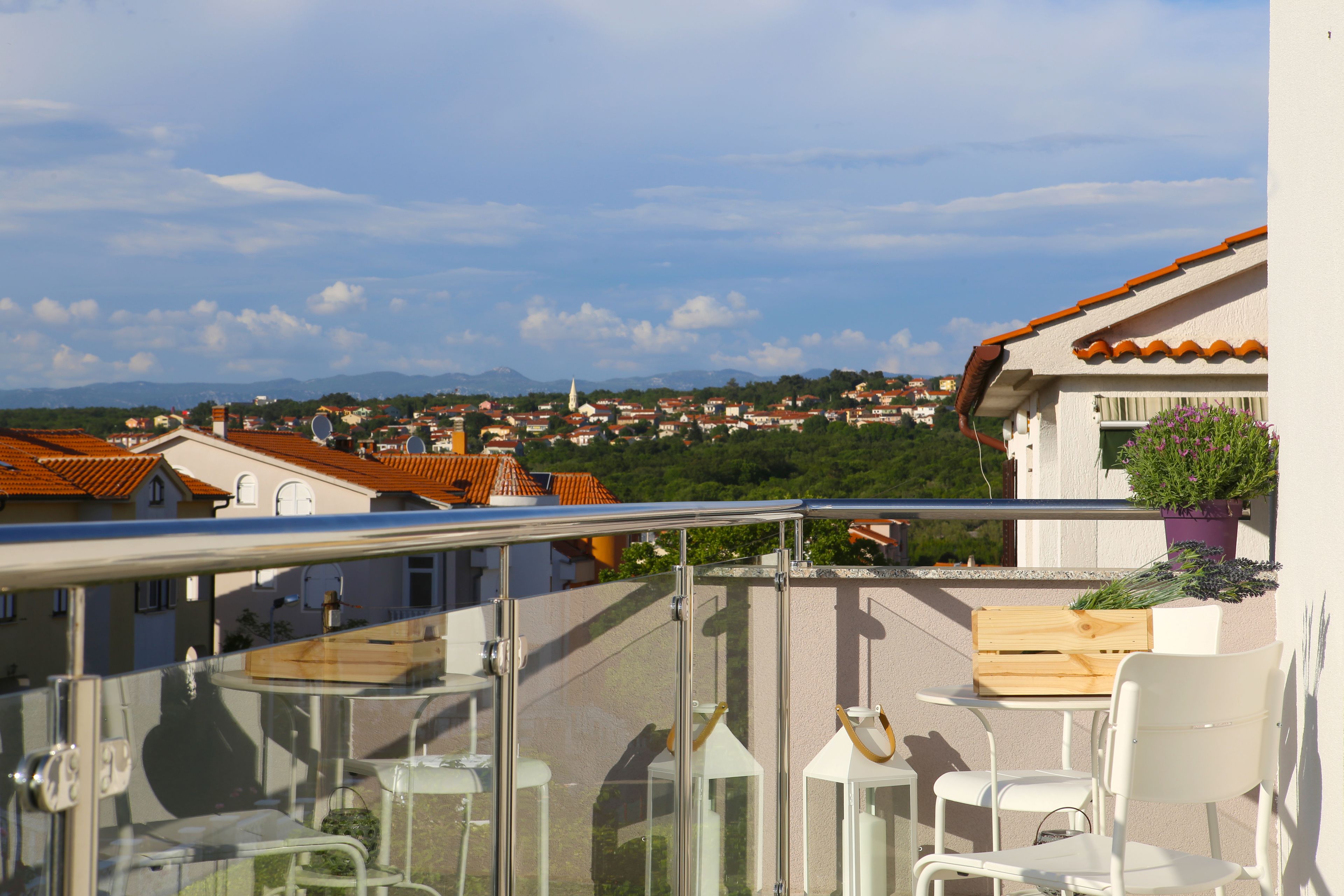 A balcony with a view of a town, a wooden crate, and a potted plant.