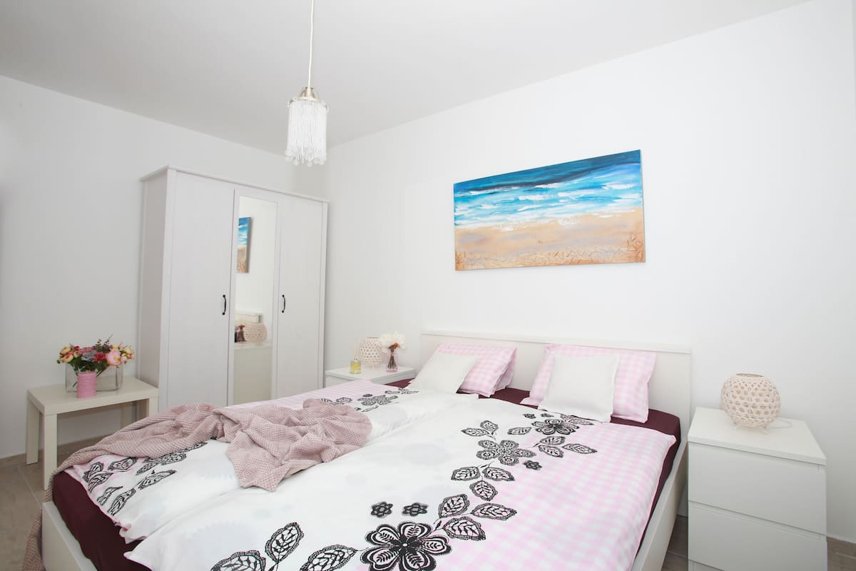 Un dormitorio con una cama, un armario blanco, mesitas de noche y un cuadro de una playa.