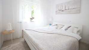 Ein Schlafzimmer mit einem großen Bett, einem Fenster mit Vorhängen, einem Nachttisch mit Lampe und einem Bild an der Wand.