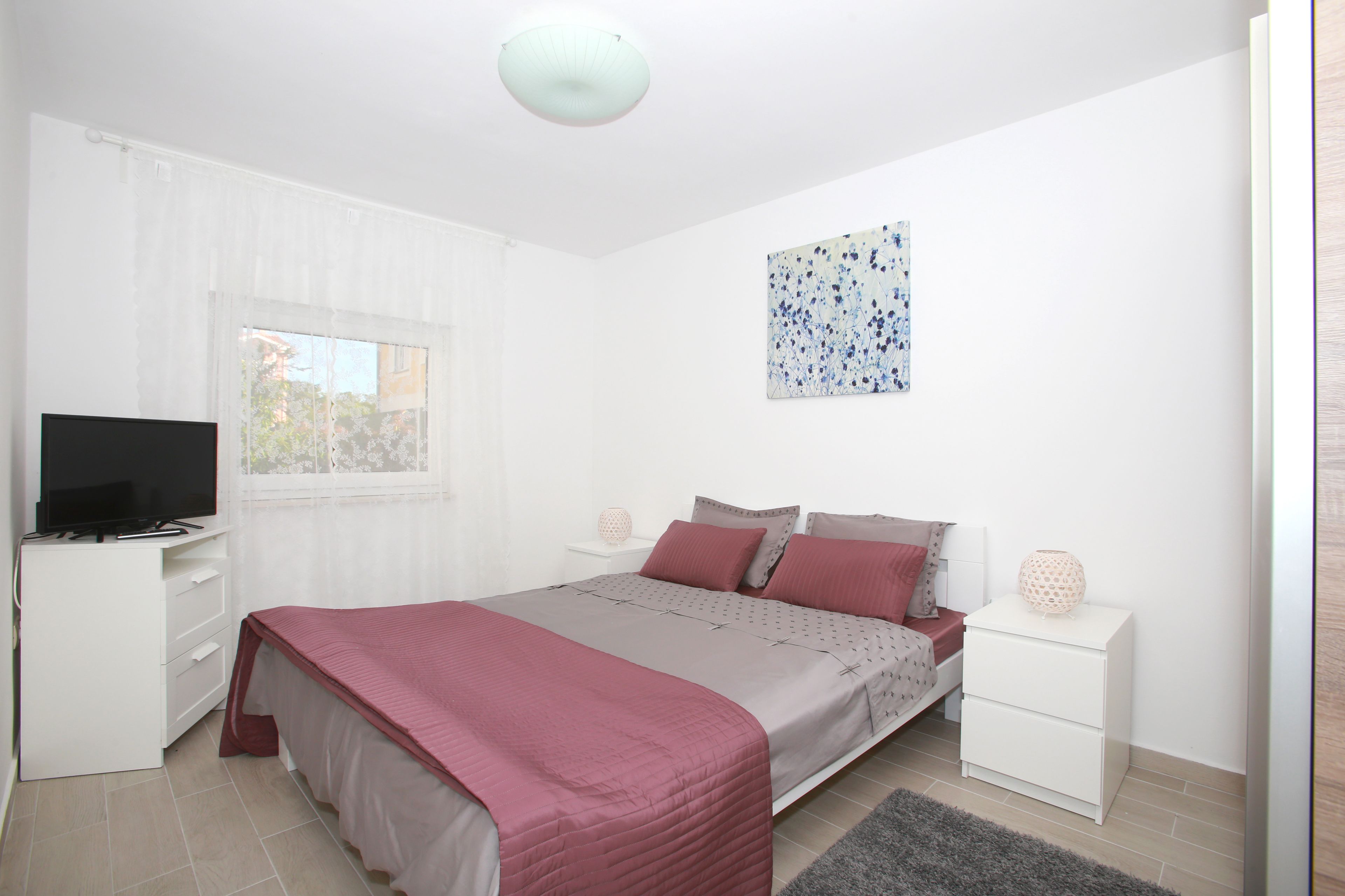 A bedroom with a bed, a TV, a desk, and a window.