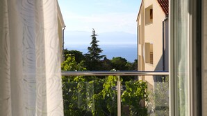 Ein Balkon mit Blick auf Meer und Berge, ein Gebäude mit Ziegeldach und ein Baum im Hintergrund.
