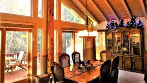 A dining area with a wooden table and chairs, large windows, and a chandelier.