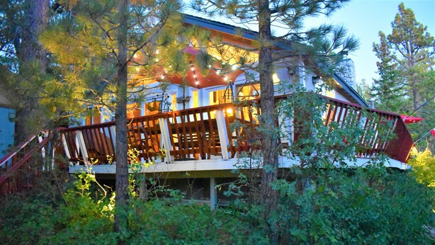 A cabin with a wooden deck, surrounded by trees and vegetation.