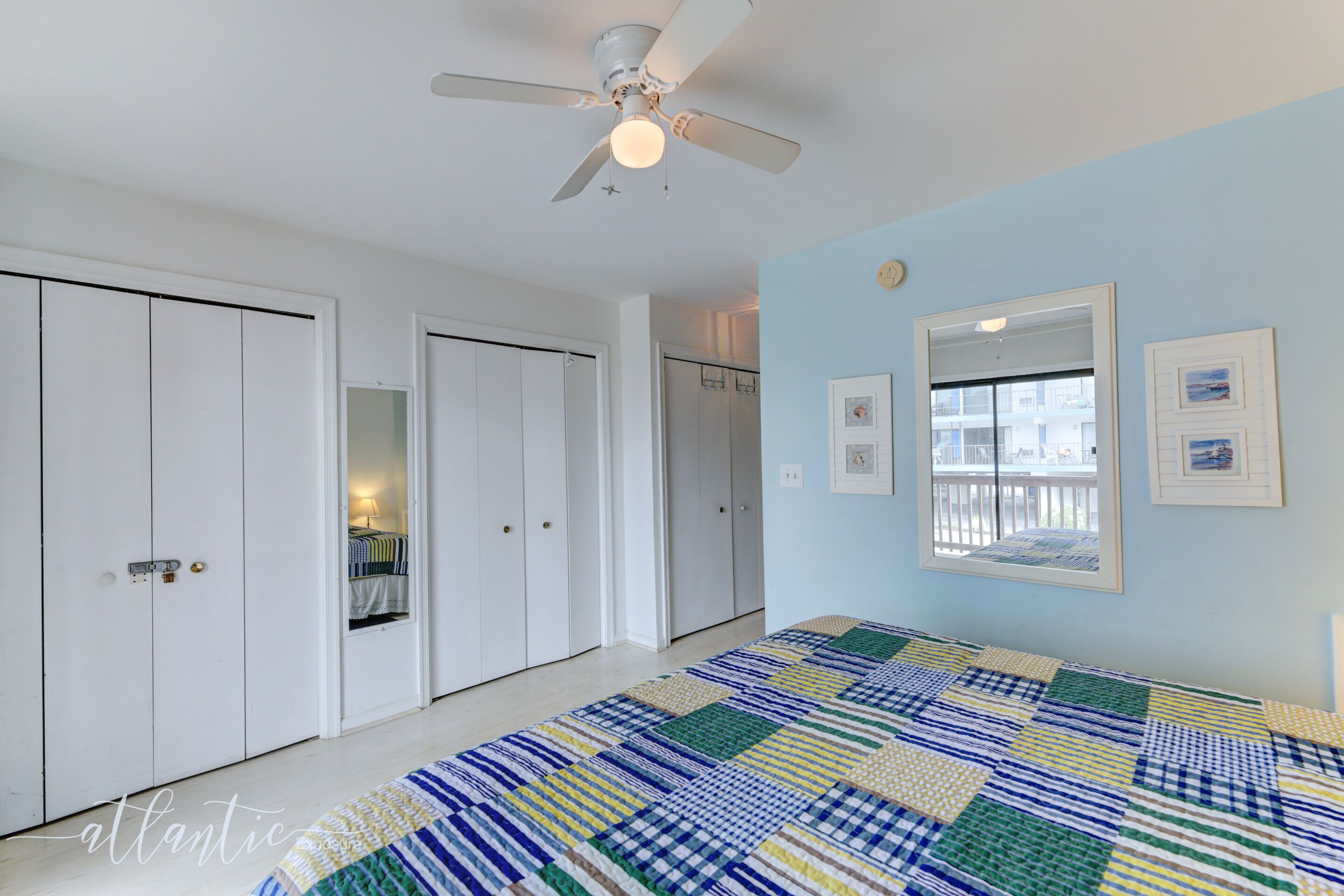 A bedroom with a large bed, a ceiling fan, and a view of the outside through a window.