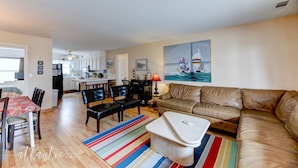 A living room with a brown leather sofa, a striped rug, a dining table with chairs, and a kitchen in the background.