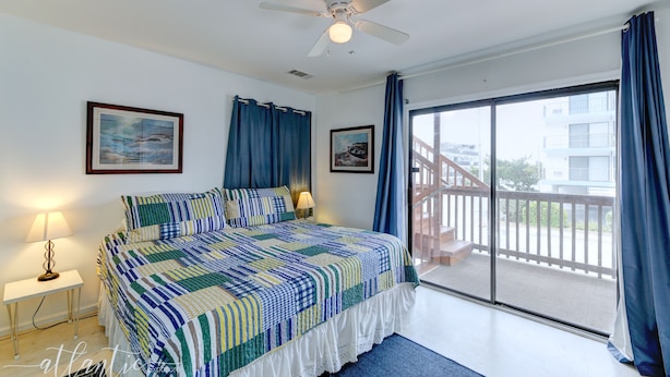 A bedroom with a large bed, a ceiling fan, a window with curtains, and a balcony with a railing.