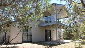 Una casa moderna de dos pisos con balcón, ventanas amplias y un patio con césped escaso.