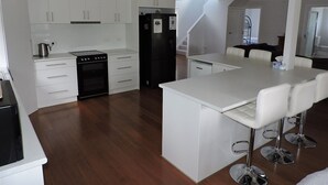 Una cocina moderna con armarios blancos, un refrigerador negro, una estufa y un comedor con sillas blancas.