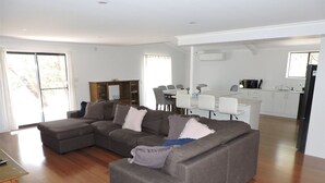 Una sala moderna con un sofá modular, un comedor con mesa y sillas, y una cocina al fondo.