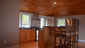 A modern kitchen with wooden cabinets, a stainless steel refrigerator, and a large island with chairs.