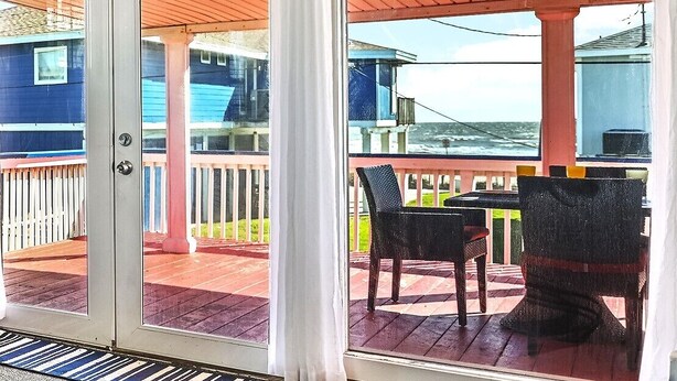 Ein überdachter Außenbereich mit Tisch und Stühlen, ein Holzdeck und Blick auf das Meer.