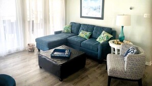 Ein Wohnzimmer mit einem Ecksofa, einem kleinen runden Tisch, einem Sessel und einem Deckenventilator.