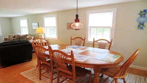 Un espace repas comprenant une table ronde en bois, six chaises en bois et un luminaire suspendu.