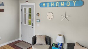Ein Zimmer mit Rattanmöbeln, einer Tür, Wanddekorationen, darunter ein Schild mit der Aufschrift 'MONOMOY', sowie einem Seestern.