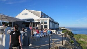 Ein Küstenrestaurant mit Außenbestuhlung und Meerblick, bewölkter Himmel und ein Schild mit der Aufschrift 'NO LITTER'.