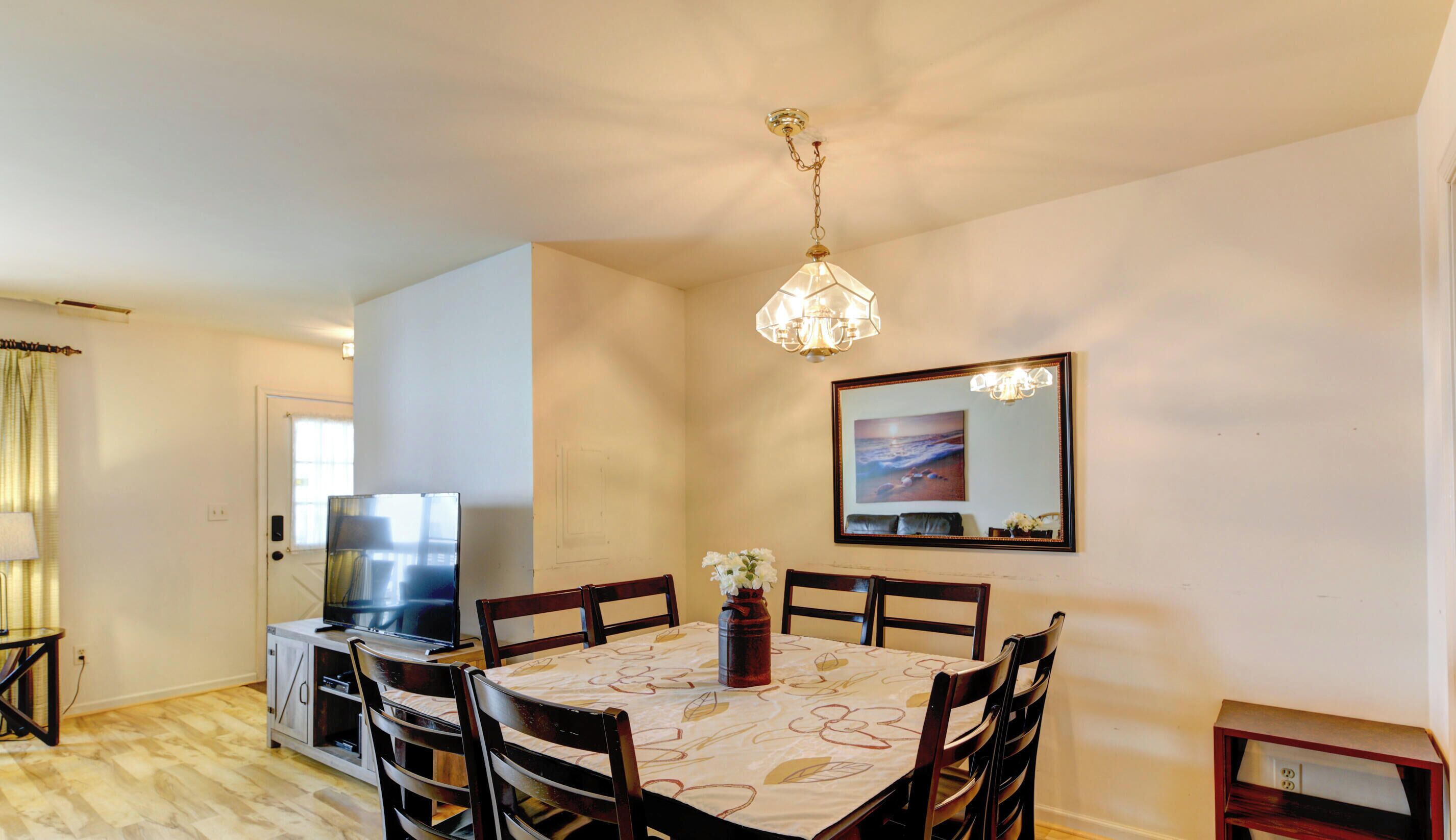 Un coin repas avec une table dressée pour quatre personnes, entourée de chaises en bois, un téléviseur posé sur un meuble et un vase décoratif rempli de fleurs.