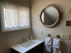 A bathroom with a sink, mirror, window with lace curtains, and two towels hanging on a towel ring. - Best location in the Valley! Walk to weddings, concerts and mountain activities (Ellicottville)