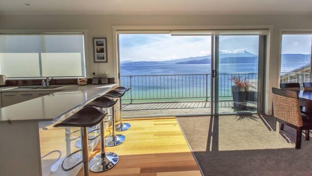 Une cuisine moderne avec un coin bar, de grandes portes-fenêtres coulissantes donnant sur un balcon avec vue sur la mer.