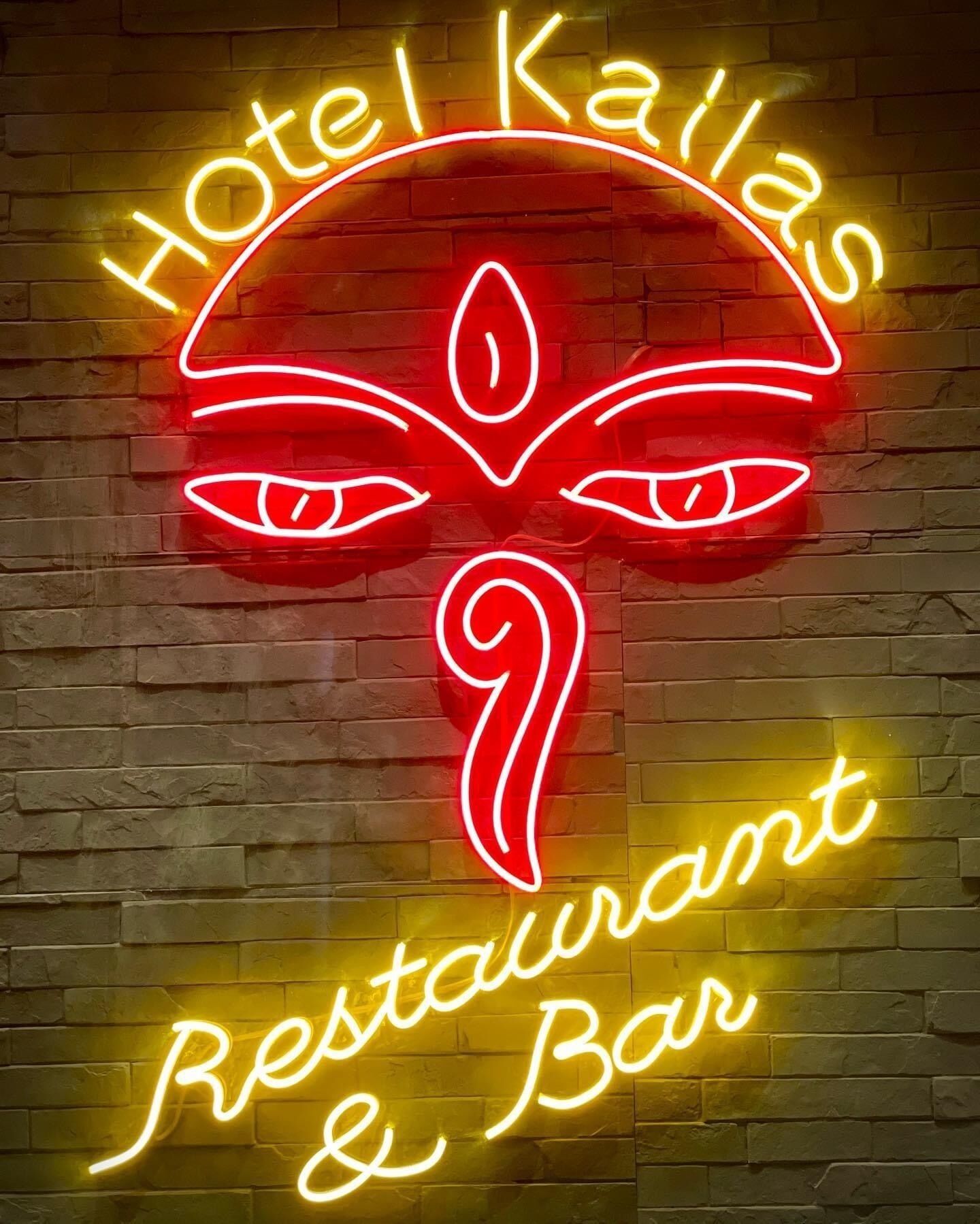 Un letrero de neón con el texto 'Hotel Kailas Restaurant & Bar' sobre una pared de ladrillo.