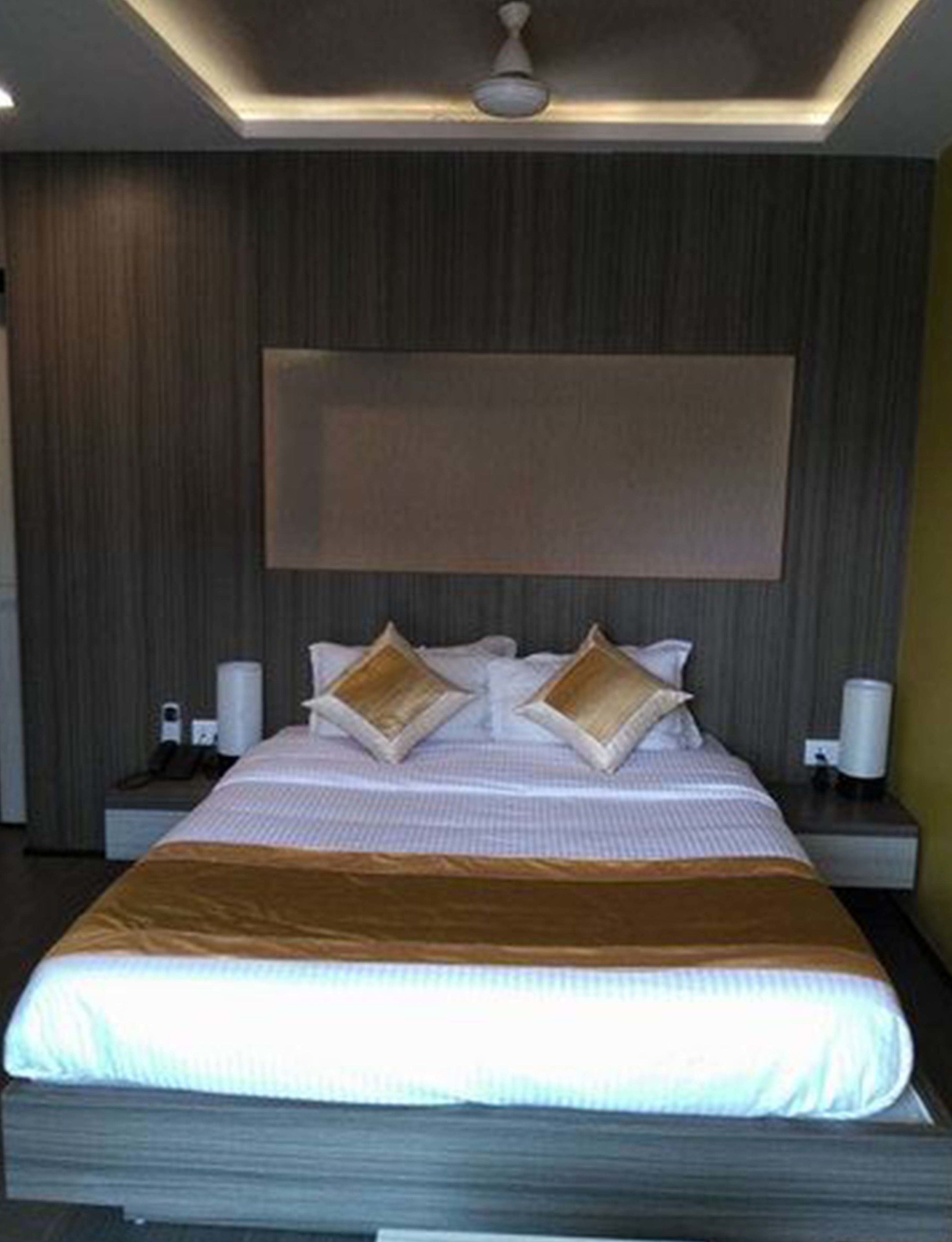 Une chambre d’hôtel moderne dotée d’un grand lit, de deux tables de chevet, d’un téléviseur fixé au mur et d’un ventilateur de plafond.