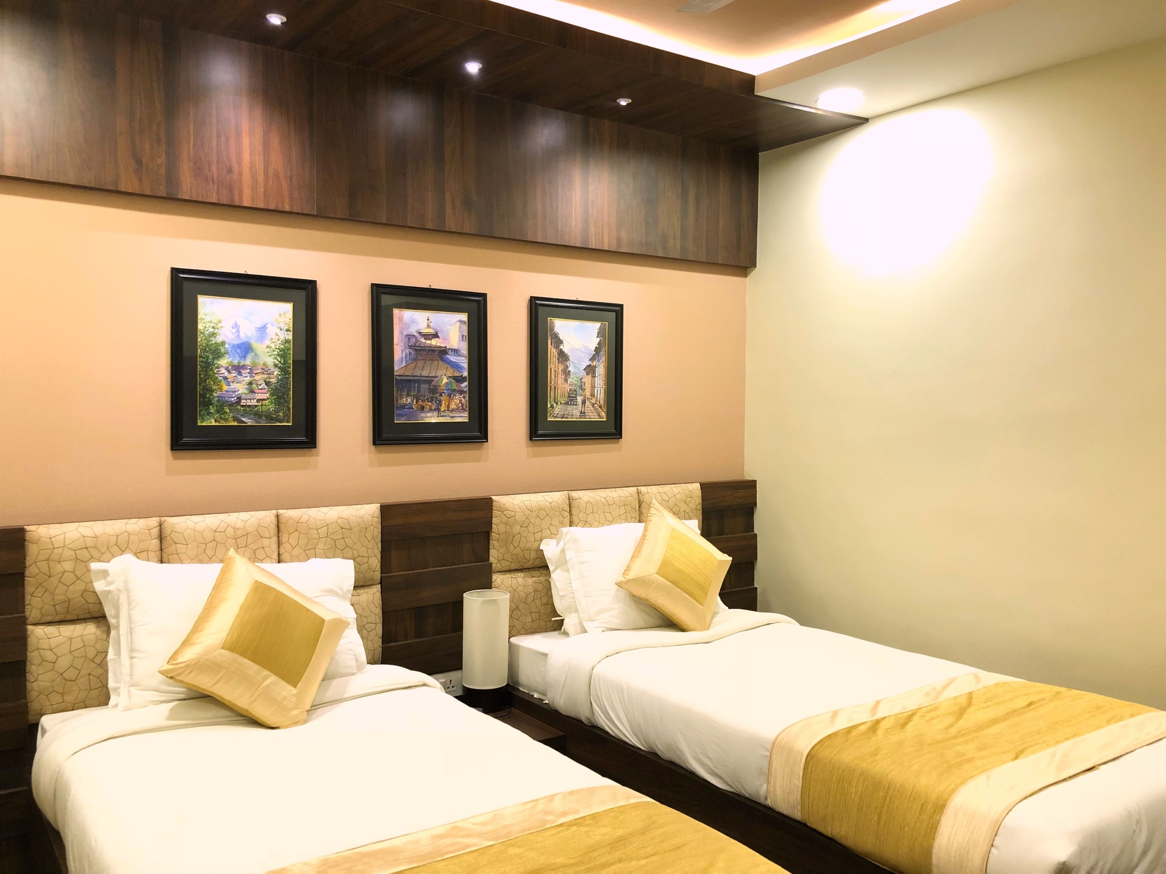 A hotel room with two beds, a wooden headboard, and three framed pictures on the wall.